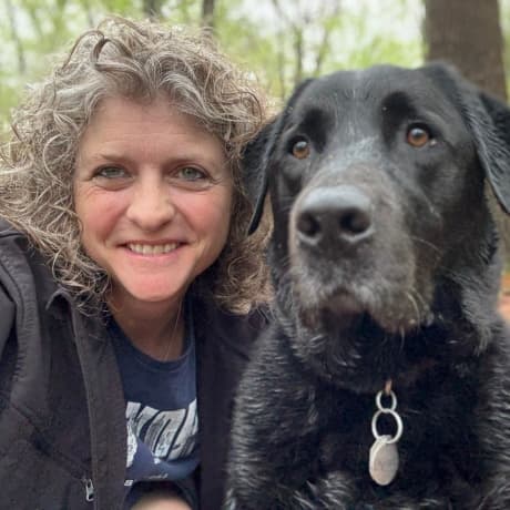 Andrea, Veterinary Assistant, cheek to cheek with her black dog Mozzie.