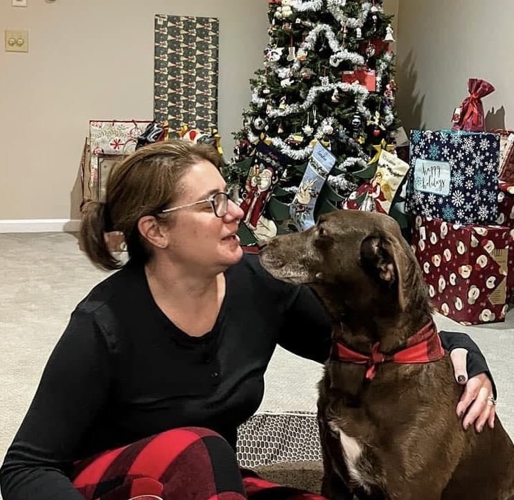 Tina, Veterinary Assistant, sitting with her brown dog beside a Christmas tree.